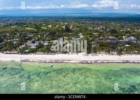 Vista aerea della spiaggia baciata dal sole con acque turchesi cristalline che incontrano la spiaggia sabbiosa fiancheggiata da palme ed edifici, Diani Beach, Kwale County, Kenya. Foto Stock
