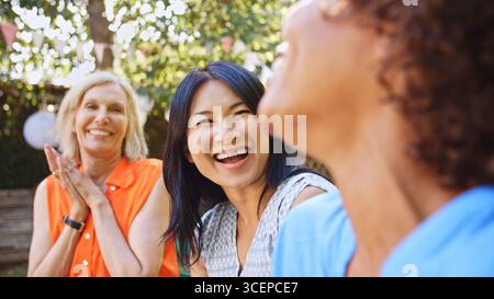 Primo piano di amiche mature e sorridenti che socializzano in Backyard Together Foto Stock
