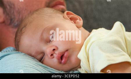 Primo piano del padre che giace sul divano a Home Cuddling Newborn Baby Son Foto Stock
