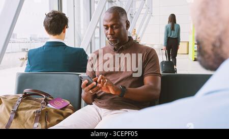 Uomo d'affari maturo seduto nella sala partenze dell'aeroporto utilizzando il telefono cellulare Foto Stock
