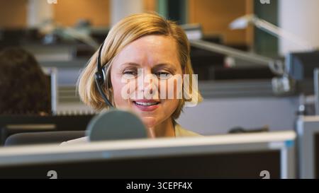 Donna d'affari matura che indossa cuffie telefoniche e lavora presso il servizio clienti Foto Stock