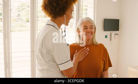 Infermiera donna che indossa l'uniforme ascoltando il torace della paziente anziana nella stanza privata dell'ospedale Foto Stock