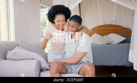 Coppia eccitata in camera da letto a casa che festeggia il risultato positivo del test di gravidanza Foto Stock