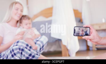 Padre che registra il video di madre e figlio seduti sul divano a casa sul telefono cellulare Foto Stock