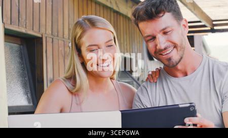 Coppia all'aperto seduti al tavolo a casa in streaming su tablet digitale a casa Foto Stock