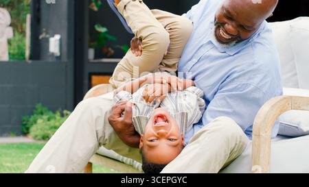 Nonno che si diverte a giocare con nipote in Garden tenendolo a testa in giù Foto Stock