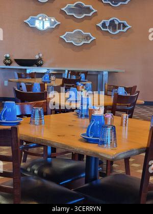 Tazze/tazze da caffè di colore blu brillante su tavoli di legno con sedie di legno; interno del ristorante in stile New Mexican all'ora della colazione Foto Stock