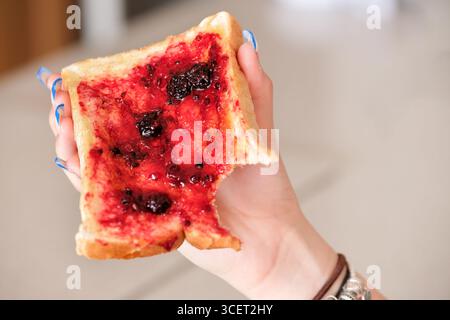 REGNO UNITO. Una persona in casa che regge una fetta di pane appena fatto con burro e marmellata di mora. Foto Stock
