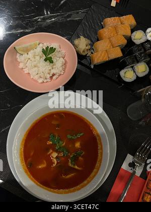 L'immagine mostra una vista dall'alto verso il basso di un tavolo con tre diversi prodotti alimentari: Una ciotola di zuppa rossa guarnita con prezzemolo, un piatto laterale con piano Foto Stock