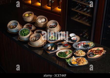 Assortimento di piatti cinesi. Spaghetti cinesi, riso fritto, gnocchi, dim sum, involtini primavera. Famosi piatti della cucina cinese su sfondo nero Foto Stock