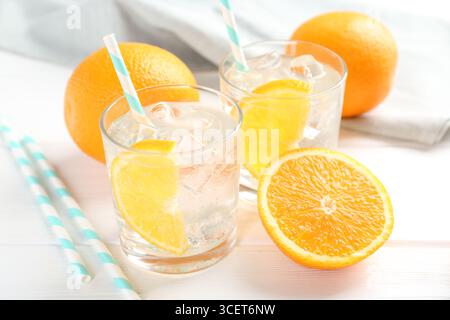 Acqua frizzante con fette d'arancia in bicchieri e frutta fresca su un tavolo di legno bianco, primo piano Foto Stock
