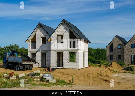 Una moderna casa a due piani in fase di costruzione iniziale, con un camion e materiali da costruzione sul sito sotto un cielo azzurro Foto Stock