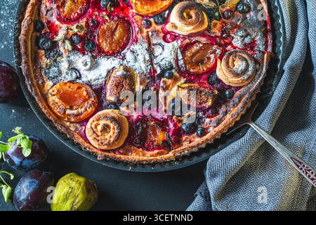 Una crostata o una torta aperta con mirtilli, fichi, prugne e albicocche in un piatto da forno su sfondo grigio. Primo piano. Foto di alta qualità Foto Stock