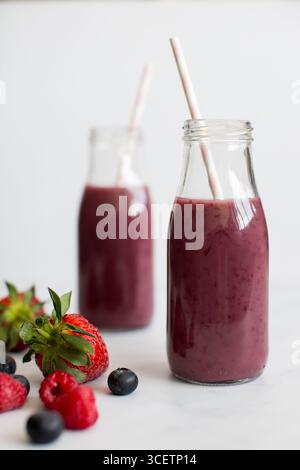 Frullato di frutti di bosco in bottiglie di vetro con cannucce di carta e fragole fresche, lamponi e mirtilli su sfondo bianco. Foto Stock