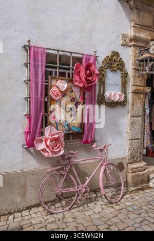 Finestra decorata e bicicletta di colore rosa di fronte al negozio di abbigliamento di Óbidos, Portogallo Foto Stock
