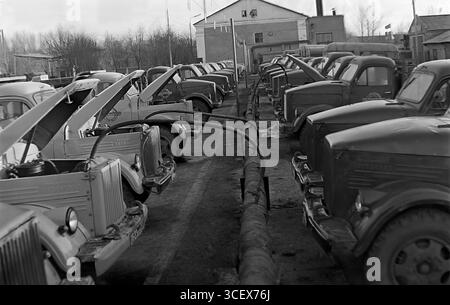 I lavoratori ispezionano i camion GAZ-51 con cappe aperte presso il parco macchine "Selkhoztekhnika" di Sloviansk, RSS Ucraina, anni '1960 - uno scenario di preparazione per la stagione della semina nel tranquillo Donbas Foto Stock