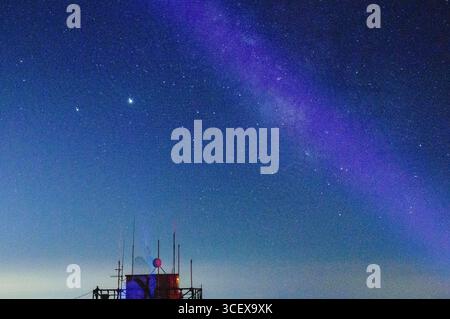 Cielo notturno con la via Lattea che si illumina sopra una stazione di telecomunicazione remota e antenne su una collina. Foto Stock