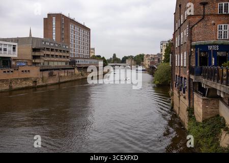 Fiume della città fiancheggiato da edifici in mattoni e appartamenti, con cigni che nuotano sull'acqua sotto un cielo nuvoloso Foto Stock
