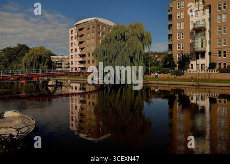 Passerella rossa e appartamenti accanto a un canale, un grande salice piangente e riflessi, persone sull'argine in una zona residenziale di Amsterdam. Foto Stock