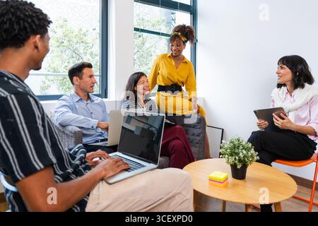 Cinque persone aziendali stanno organizzando riunioni produttive in un ufficio moderno, utilizzando notebook e tablet, discutendo idee e strategie per la loro startup Foto Stock