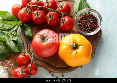 Pomodori a bordo con pepe e rametto di basilico su sfondo azzurro. Primo piano Foto Stock