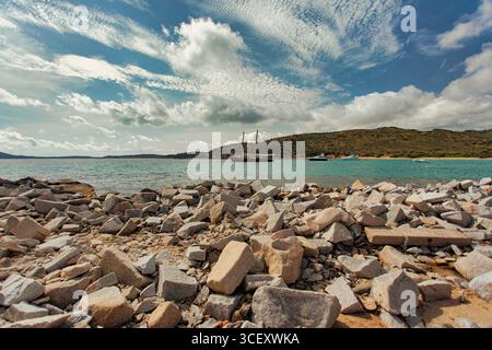Punta molentis, italia 20 agosto 2025: Barca a vela ancorata vicino a una spiaggia rocciosa a punta molentis, in sardegna, sotto un cielo nuvoloso Foto Stock