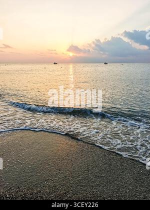 Tranquilla spiaggia all'alba, caratterizzata da dolci onde che si infrangono sulla spiaggia sabbiosa, con colori vibranti che si riflettono nel cielo e nell'acqua, creando Foto Stock
