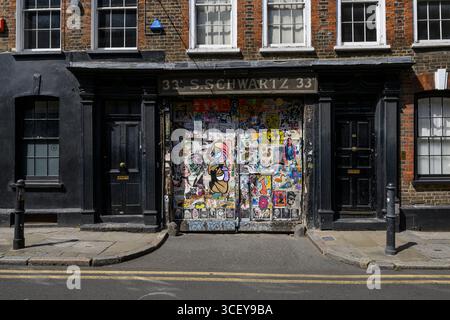 Porte coperte da poster in pasta di grano Street art, Fournier Street, Londra, Regno Unito. 12 giugno 2025 Foto Stock