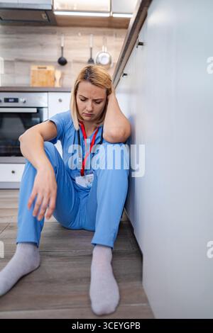Dottore esausto seduto sul pavimento in cucina Foto Stock