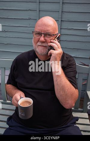 Vecchio con il caffè sullo smartphone. uomo anziano e tecnologia in uso Foto Stock