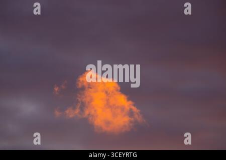 Una singola nuvola arancione che si illumina al tramonto contro il cielo scuro Foto Stock