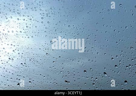 Gocce di pioggia sulla finestra di vetro con cielo nuvoloso. Primo piano di goccioline d'acqua su una superficie di vetro trasparente durante le precipitazioni, con un cielo coperto di umidità nel Foto Stock