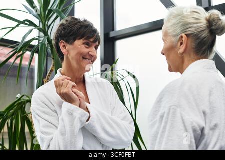 Due belle donne mature condividono una conversazione gioiosa in un centro benessere incentrato sulla cura di sé. Foto Stock