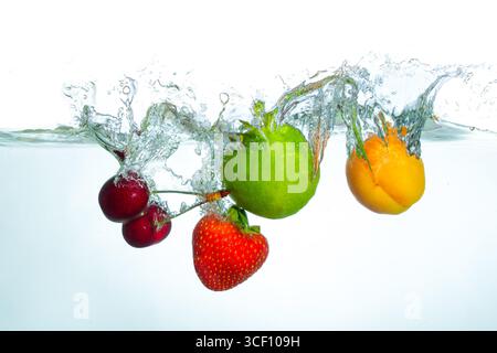 Frutti vivaci, tra cui ciliegie, lime, albicocche e fragole che spruzzano in acqua limpida, creando schizzi dinamici e riflessi sotto una liscia luminosa Foto Stock