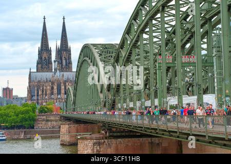 Colonia, Germania - 15 giugno 2025: Vista del ponte Hohenzollern con la cattedrale di Colonia sullo sfondo, che cattura l'atmosfera vivace di un trambusto Foto Stock