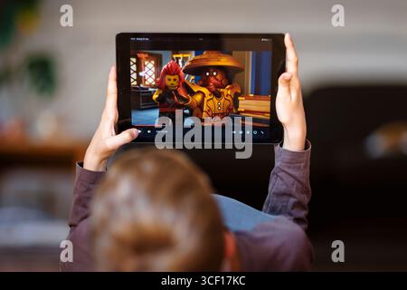 Berlino, Germania. 18 agosto 2025. Foto simbolica: Immagine basata sui gesti sul tema dell'uso dei media tra i bambini. Un bambino giace sul pavimento di casa, guardando un cartone animato di Lego Ninjago su un tablet. Berlino, 18 agosto 2025. Credito: dpa/Alamy Live News Foto Stock