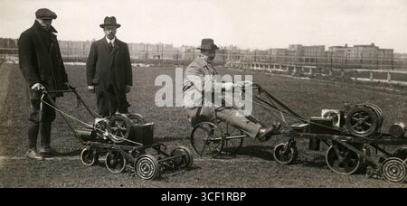 Nel 1924, tre uomini sono visti con due tosaerba motorizzati in un campo, uno dei quali è attaccato a una sedia, probabilmente per facilità di funzionamento, con condomini visibili sullo sfondo. Foto Stock