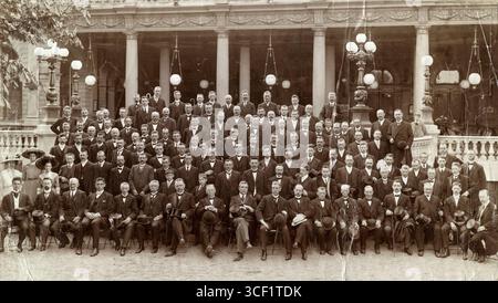 Una foto di gruppo di tutto il personale della Rotterdam Verzekerings Sociëteit (RVS) che lavorava fuori Rotterdam, si è riunito per un giubileo nel 1911. La foto mostra circa un centinaio di uomini e tre donne con un colonnato e lampade rotonde sullo sfondo. Foto Stock