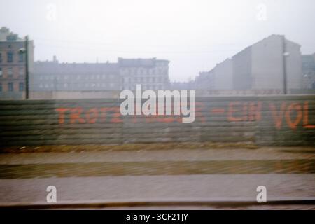 Graffiti che recitano "Trotz Mauer - Ein Volk" sul muro di Berlino vicino al Checkpoint Charlie, aprile 1963. Foto scattata da un'auto in movimento. Foto Stock