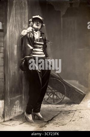 Una donna vestita da ragazzo malizioso con pantaloni a pieghe di raso, una camicia a righe, una giacca in raso e un berretto a un ballo in maschera all'Opera di Parigi nel 1923. La fotografia cattura lo spirito giocoso delle palle in costume. Foto Stock