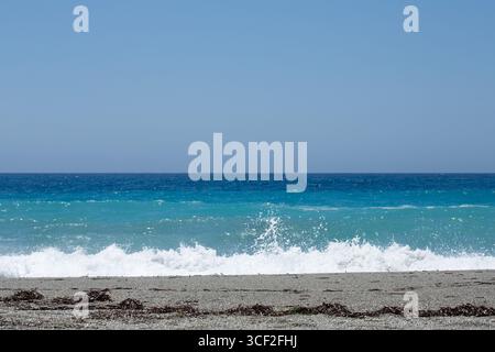 Onde dolci che si infrangono su una spiaggia sabbiosa con acque turchesi che si incontrano con un cielo azzurro limpido in una giornata estiva Foto Stock
