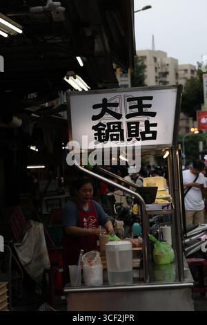 TAIPEI, TAIWAN. 1° GIUGNO 2024. Un venditore ambulante prepara la guotie (gnocchi fritti in padella) sotto un cartello luminoso con la scritta "da Wang Guotie", catturando il vivace Foto Stock