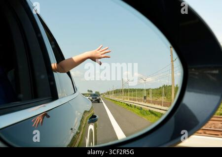 Mano di una donna sullo specchietto retrovisore di un'auto sulla strada Foto Stock