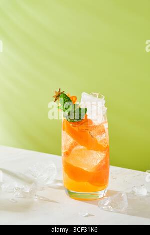 Cocktail freddo rinfrescante all'arancia e al lime guarnito con foglie di menta e timo in vetro su sfondo verde chiaro. Drink estivi a casa. Foto Stock