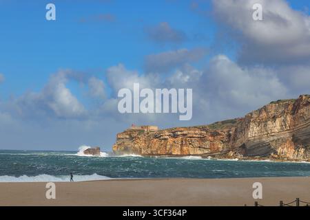 Onde che si infrangono sotto il promontorio e il forte de Sao Miguel Arcanjo a Nazare, Portogallo. Foto Stock