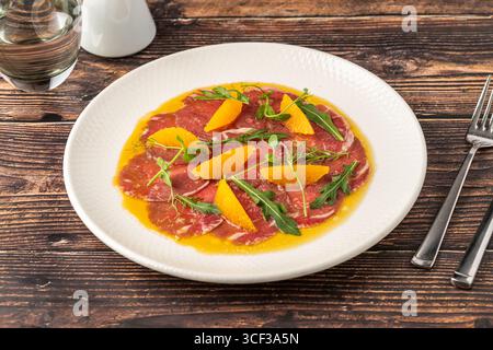 Carpaccio di manzo a fette sottili con segmenti di arancia e foglie di rucola Foto Stock