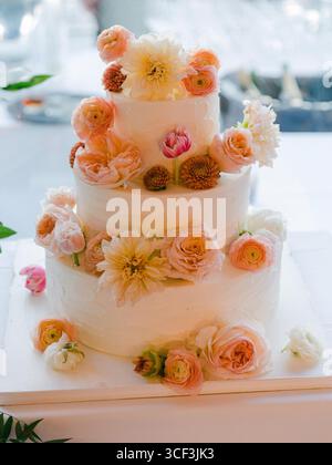 Una stupenda torta nuziale decorata con fiori vivaci, elegantemente esposta a festeggiamenti gioiosi. Foto Stock