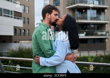 Una coppia interrazziale amorevole condivide un bacio tenero all'aperto Foto Stock