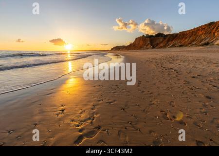 Splendida spiaggia sabbiosa con rocce rosse e scogliere, crepuscolo al tramonto con onde poco profonde sulla costa atlantica a Praia do poco Velho, Praia da Falesia, Algarve, Portogallo Foto Stock