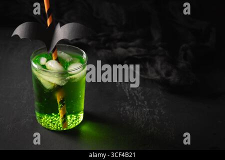 Cocktail verde Halloween guarnire pistrello nero su sfondo nero. Drink festivi e decorazioni festose. Primo piano. Foto Stock
